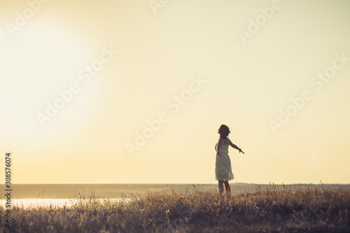 Woman watching the sunset in a long white dress on the coast of the lake. photo from the back, without a face. Selective focus.