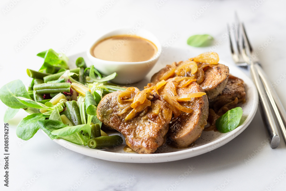 Fried juicy pork chops with caramelized onion and sauce served with green salad and beans. Light grey background, selective focus. Fried juicy pork chops with caramelized onion and sauce served with green salad and beans. Light grey background, selective focus.