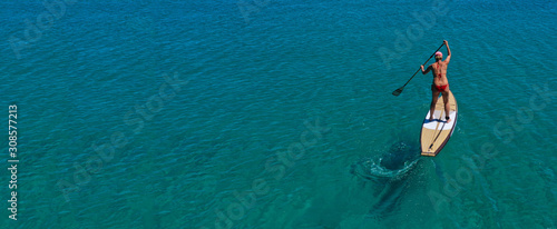 Aerial drone ultra wide panoramic photo of unidentified fit woman practising in Stand Up Paddle board or SUP in tropical island exotic turquoise bay © aerial-drone
