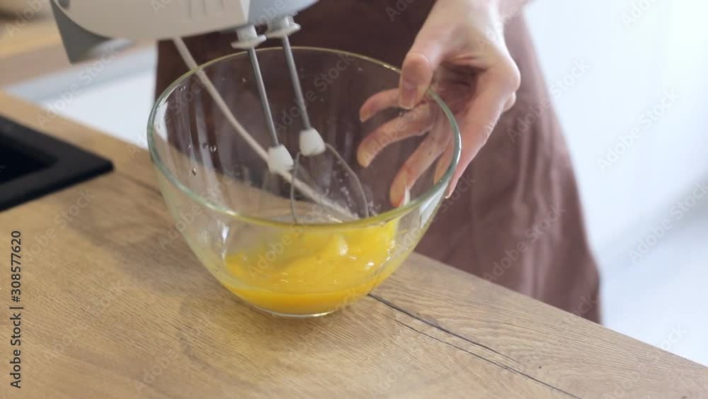 Woman in apron beating eggs with mixer in bowl Woman in apron beating eggs with mixer in bowl