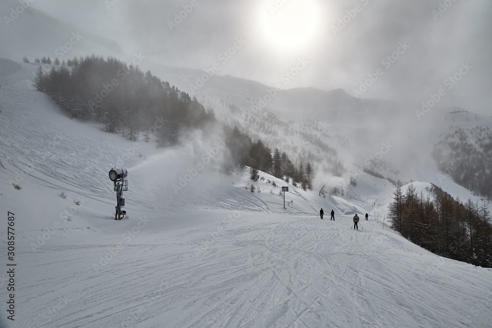 Skiing slope in the French Alps, cloudy misty weather, snow machines working