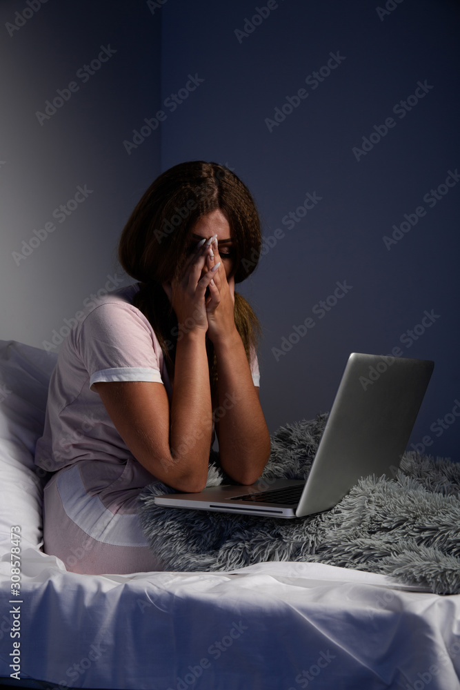 Frustrated woman in tence working on a laptop at home sitting in the bed Frustrated woman in tence working on a laptop at home sitting in the bed