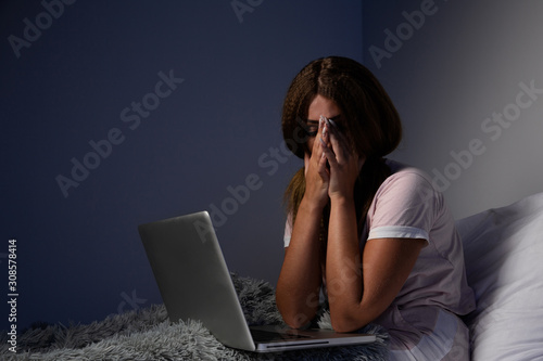 Sad unhappy female with laptop in the bed