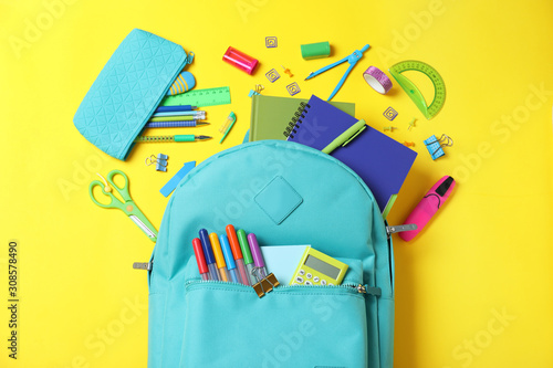 Stylish backpack with different school stationery on yellow background, flat lay photo