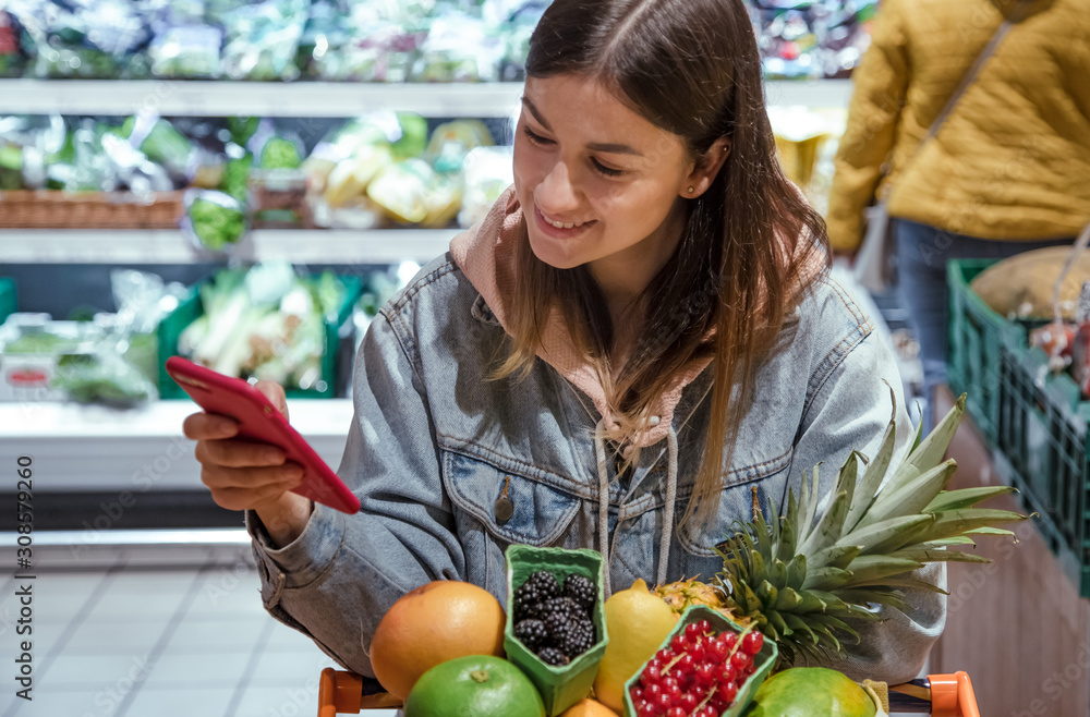 A young woman buys groceries in a supermarket with a phone in her hands. A young woman buys groceries in a supermarket with a phone in her hands.