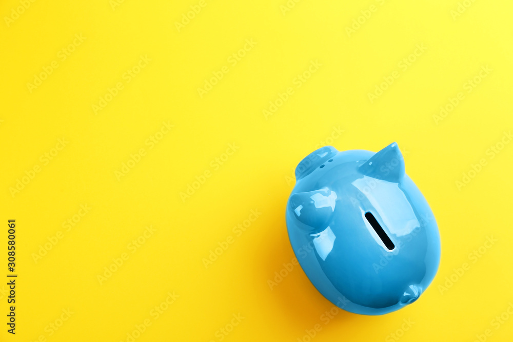 Blue piggy bank on yellow background, top view. Space for text - obrazy, fototapety, plakaty 