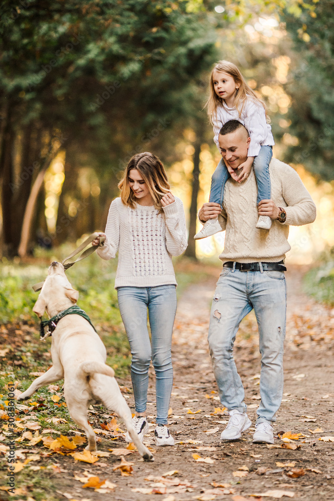 Fototapeta premium Happy beautiful family with dog labrador is having fun together walking the in park.