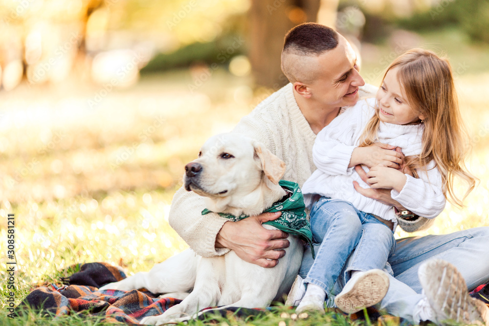 Happy father and daughter with dog labrador is having fun are sitting on green grass in park. Happy father and daughter with dog labrador is having fun are sitting on green grass in park.