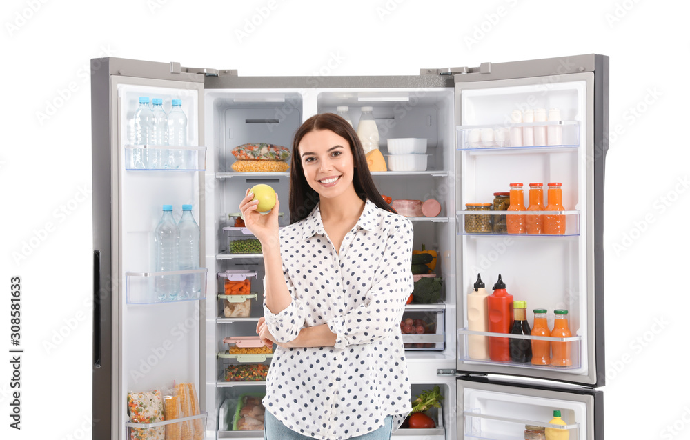 Young woman with apple near open refrigerator on white background Young woman with apple near open refrigerator on white background