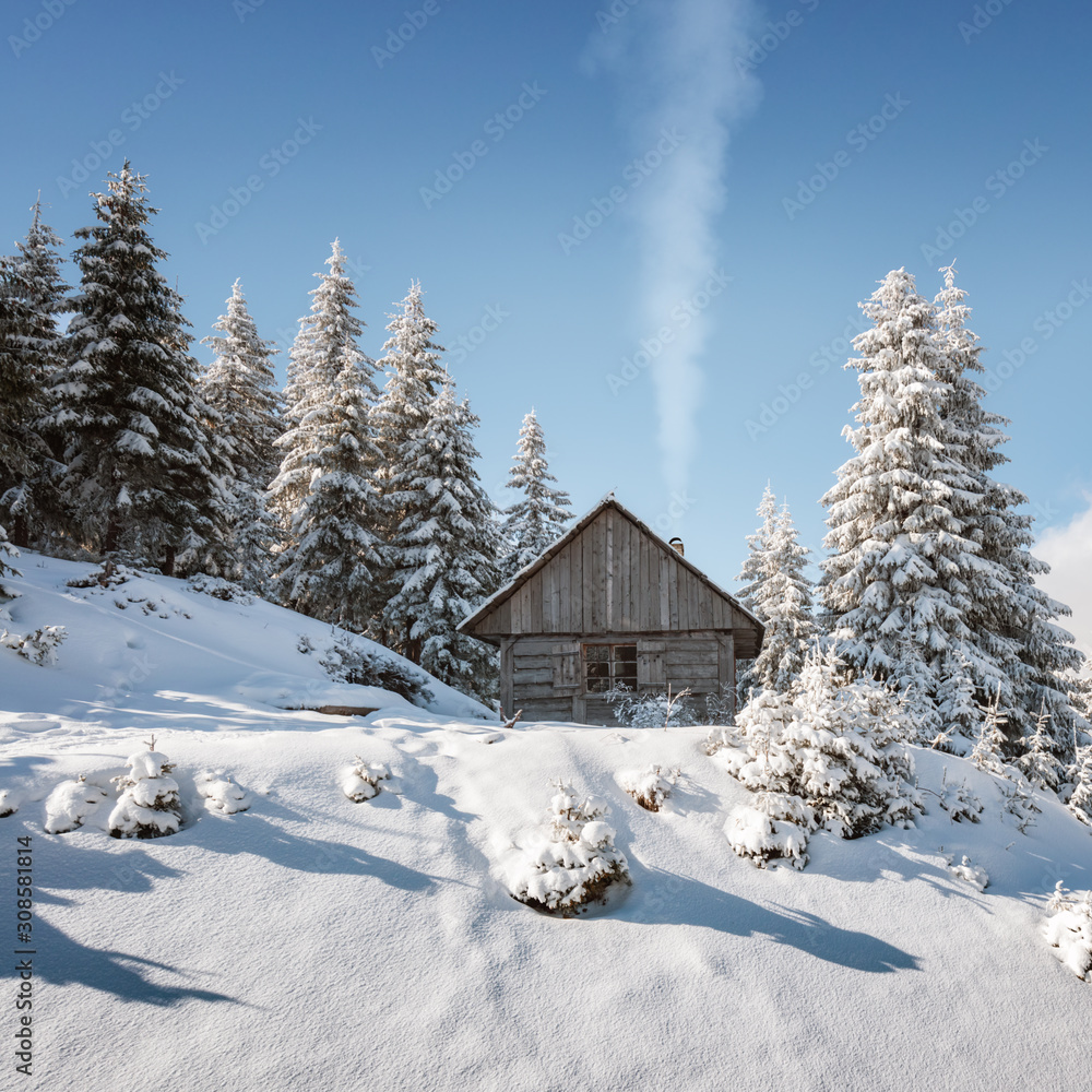 Fantastic winter landscape with wooden house in snowy mountains. Smoke comes from the chimney of snow covered hut. Christmas holiday concept Fantastic winter landscape with wooden house in snowy mountains. Smoke comes from the chimney of snow covered hut. Christmas holiday concept