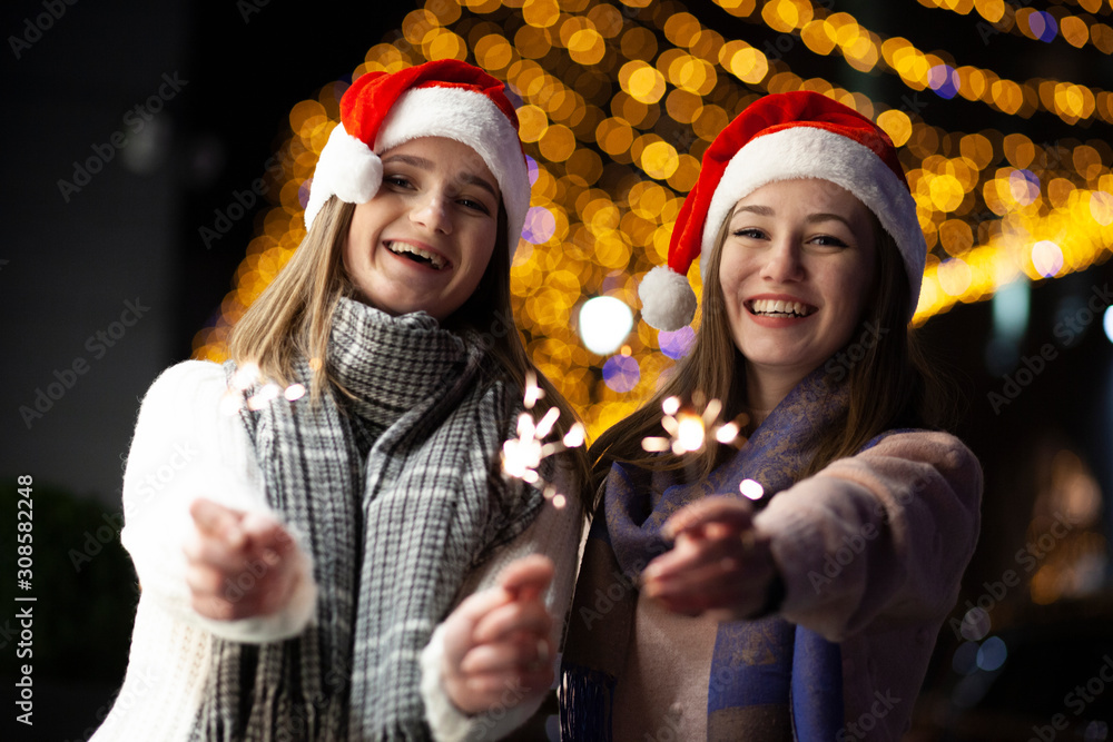 Fototapeta premium girls set fire to sparklers at night on the street, a couple of lesbians celebrate the New Year together