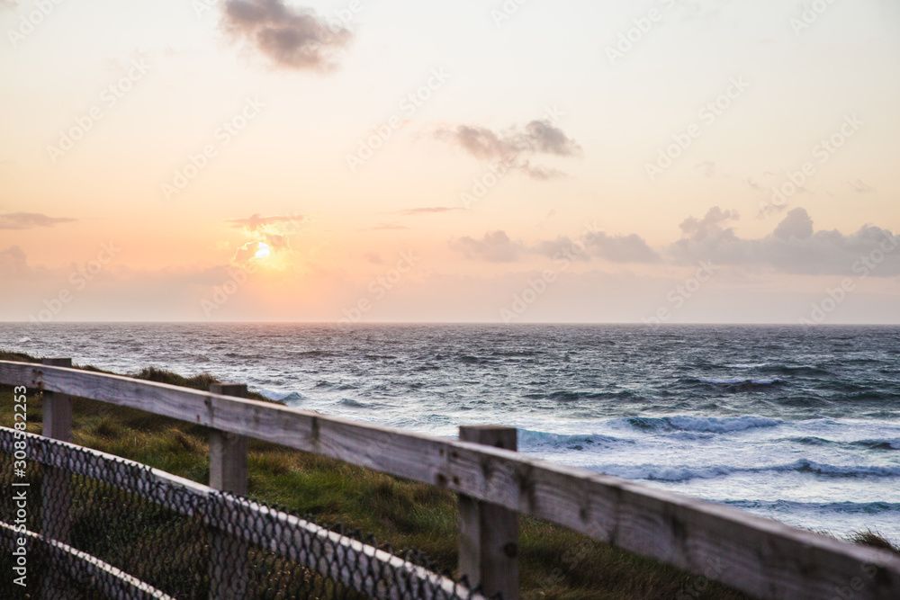 Lovely Beautiful Sunset in Cornwall England waves crashing against the base of the tall dangerous cliffs, fenced off to prevent suicide of young people or accidental death from falling.