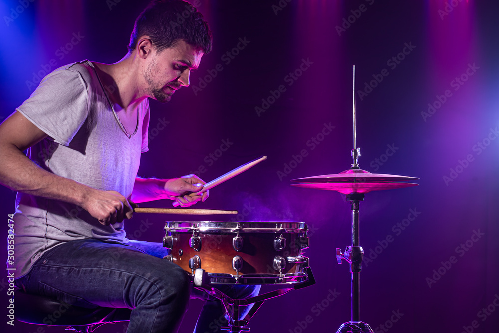 Naklejka premium The drummer plays the drums. Beautiful blue and red background, with rays of light. Beautiful special effects smoke and lighting. The process of playing a musical instrument. Close-up photo.