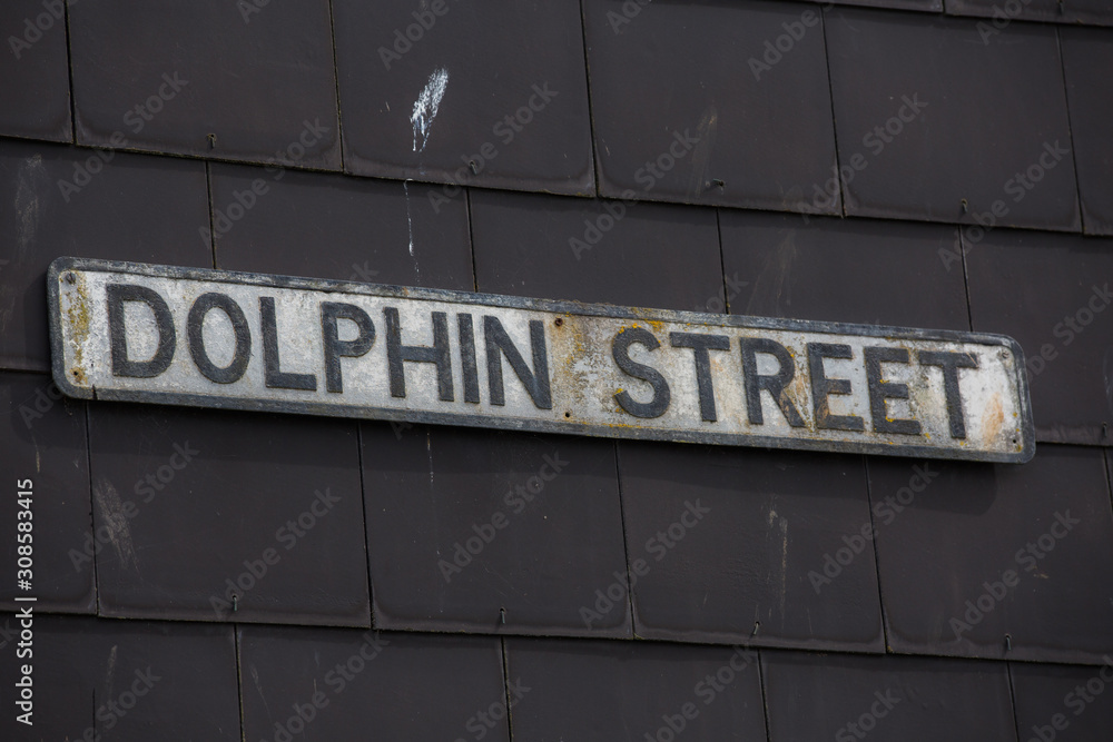 Obraz premium DOLPHIN STREET street sign on an old textured black tile wall. Funny or strange street sign in england uk. Ironic having this name on a road by the ocean where you can find the animal