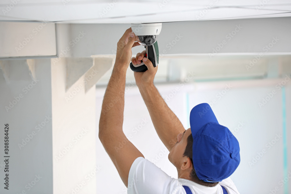 Technician installing CCTV camera on ceiling indoors Technician installing CCTV camera on ceiling indoors
