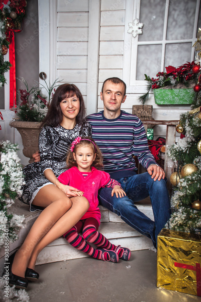 family dad mom and daughter sitting on the steps of the house with Christmas decor family dad mom and daughter sitting on the steps of the house with Christmas decor