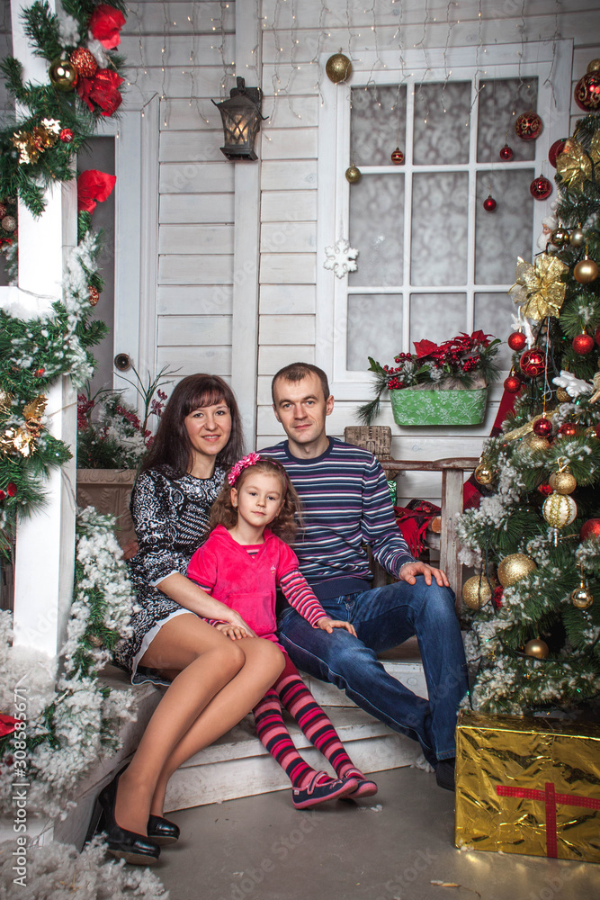 family dad mom and daughter sitting on the steps of the house with Christmas decor family dad mom and daughter sitting on the steps of the house with Christmas decor