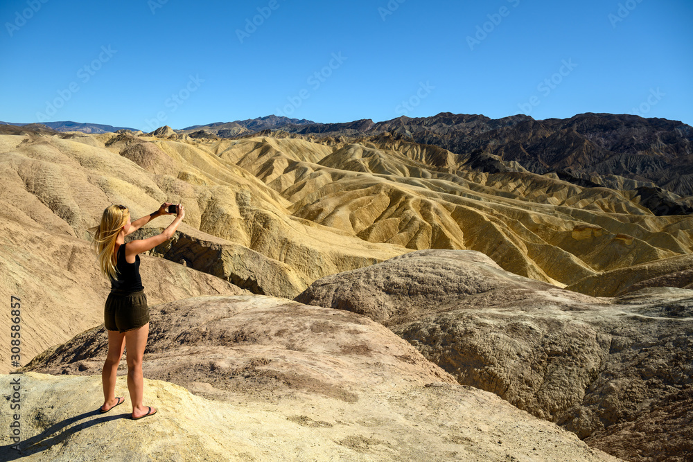Naklejka premium Attractive blonde woman standing in the landscape at Zabriskie Point, Death Valley National Park, California, USA