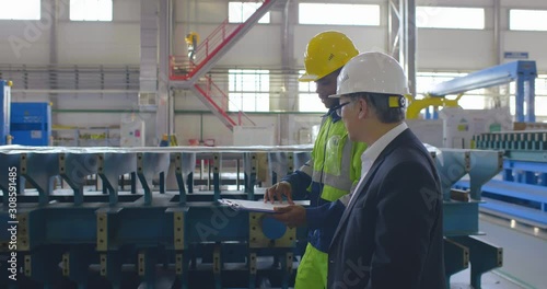 Two heavy industry workers walk through modern factory. Engineer in formal suit and worker in uniform go talking in large facility for energy industry products