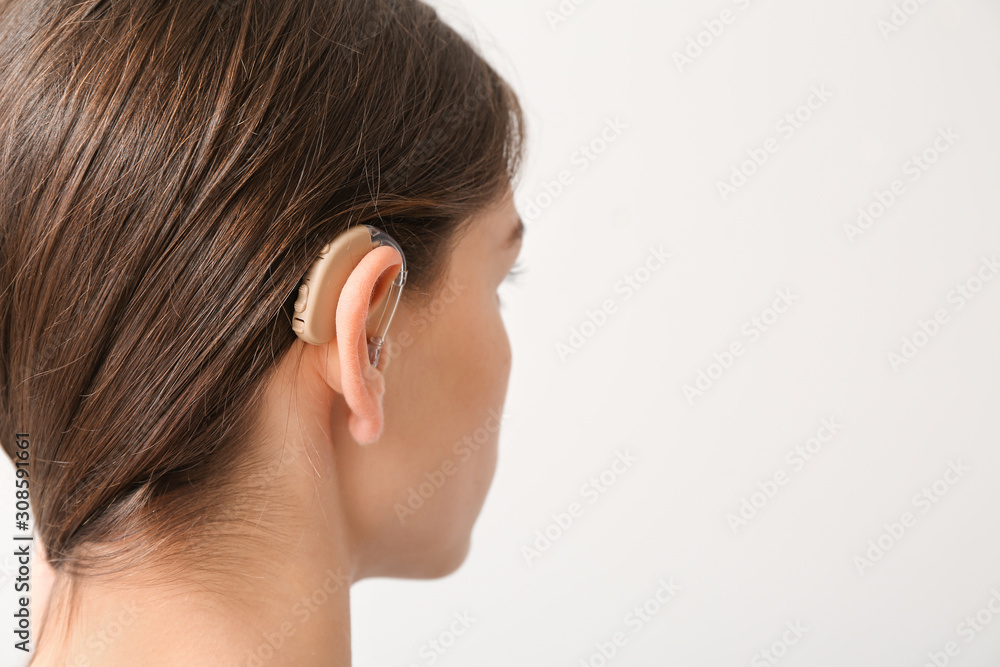 Young woman with hearing aid on light background Young woman with hearing aid on light background