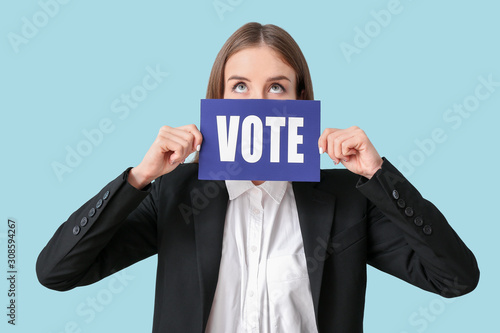 Young businesswoman holding paper with text VOTE on color background