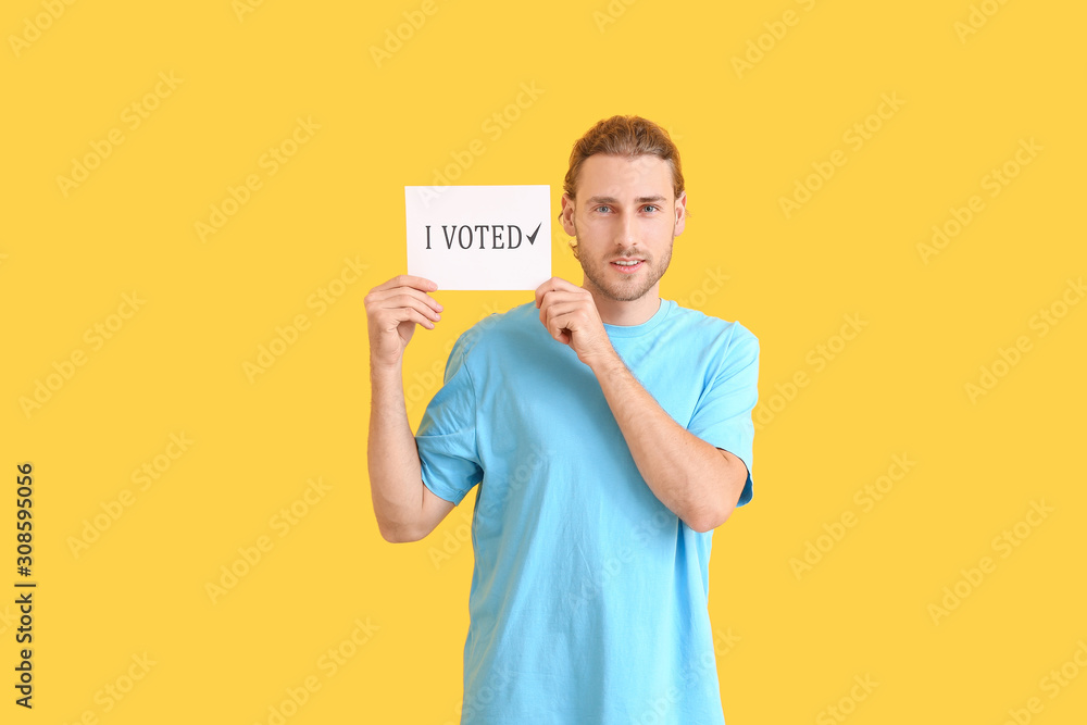 Young man holding paper with text I VOTED on color background Young man holding paper with text I VOTED on color background
