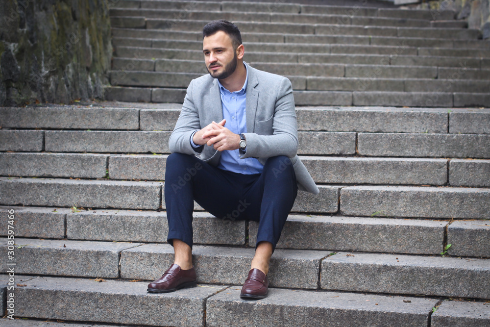 Portrait of a bearded man near the big steps of an old European castle. Businessman thinking over a future project. Fashionable guy with stylish clothes.