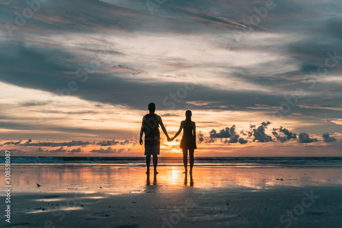 BALI, Indonésia: silhueta de casal, de mãos dadas, no por do sol da praia de Seminyak.