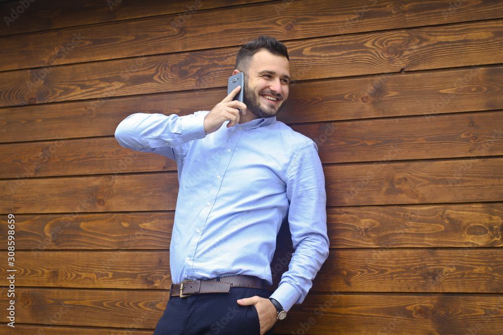 Portrait of a handsome man in a shirt on a wooden wall background. Businessman, boss in stylish clothes. Sexy guy talking on the phone. Stock Photo design Portrait of a handsome man in a shirt on a wooden wall background. Businessman, boss in stylish clothes. Sexy guy talking on the phone. Stock Photo design