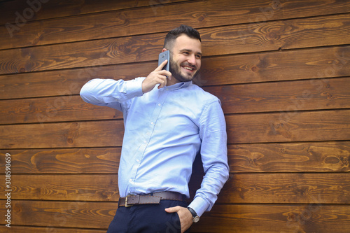 Portrait of a handsome man in a shirt on a wooden wall background. Businessman, boss in stylish clothes. Sexy guy talking on the phone. Stock Photo design
