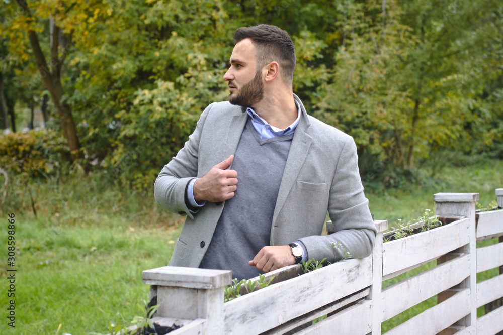 Portrait of a sexy man dressed in a suit. Fashionable guy in the autumn nature near a white wooden fence. Businessman relaxes. Skok photo for design Portrait of a sexy man dressed in a suit. Fashionable guy in the autumn nature near a white wooden fence. Businessman relaxes. Skok photo for design