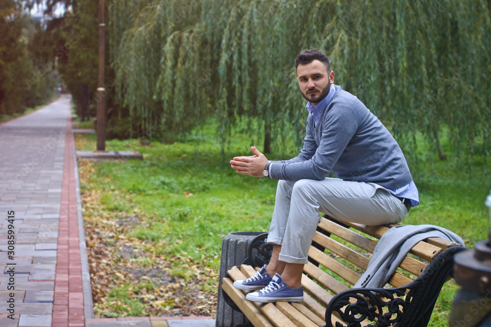 Fototapeta premium Young sexy guy sitting on a bench in an autumnal, summer park. A man contemplating new ideas while walking. European countryside. Stock Photo