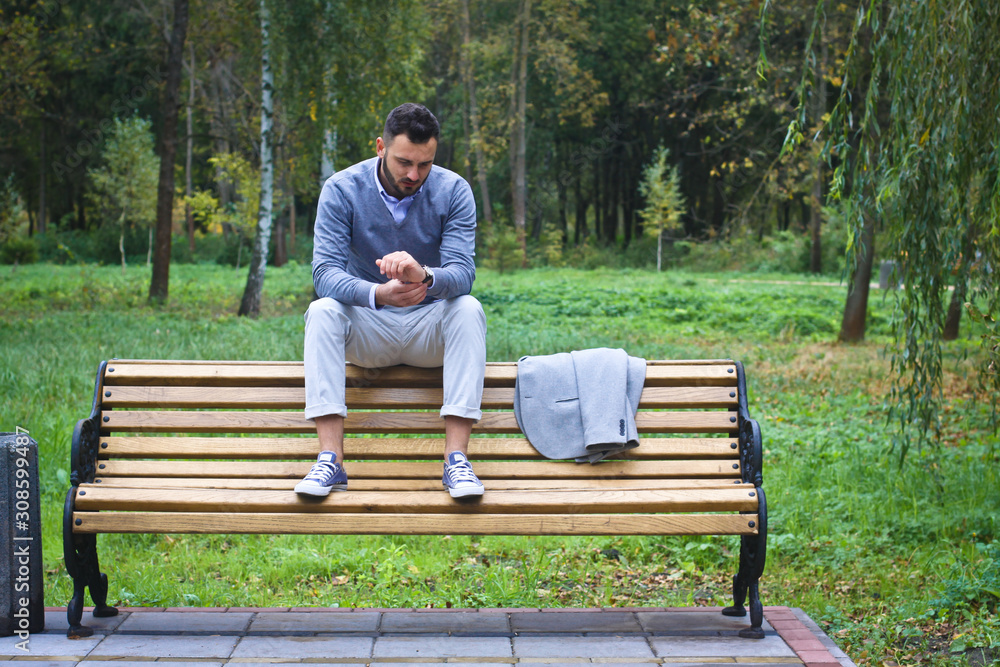Young sexy guy sitting on a bench in an autumnal, summer park. A man contemplating new ideas while walking. European countryside. Stock Photo Young sexy guy sitting on a bench in an autumnal, summer park. A man contemplating new ideas while walking. European countryside. Stock Photo