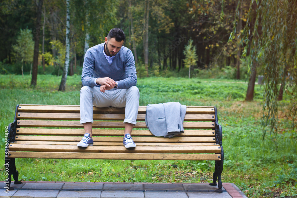 Young sexy guy sitting on a bench in an autumnal, summer park. A man contemplating new ideas while walking. European countryside. Stock Photo Young sexy guy sitting on a bench in an autumnal, summer park. A man contemplating new ideas while walking. European countryside. Stock Photo