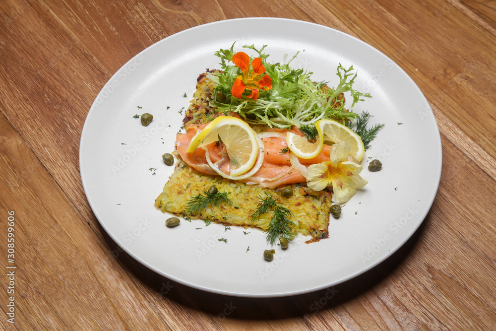 Smoked salmon with potato fritter, decorated with green salad and lemon slices. Exquisite dish. Creative restaurant meal concept. Smoked salmon with potato fritter, decorated with green salad and lemon slices. Exquisite dish. Creative restaurant meal concept.