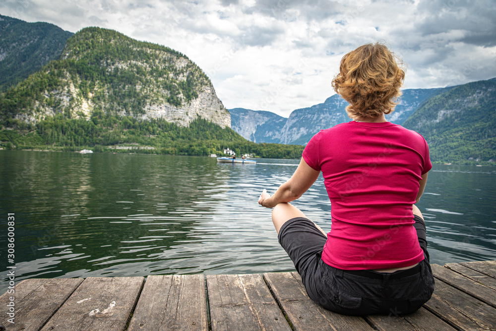 Fototapeta premium woman relaxing at lake on pier in beautiful landscape with view of mountains, lake and blue sky