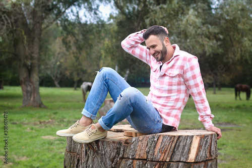 Young handsome guy Cowboy. farmer is sitting on a large stump on his ranch. Rural landscapes, countryside. Trees, field, farm. Stock photos for design. photo