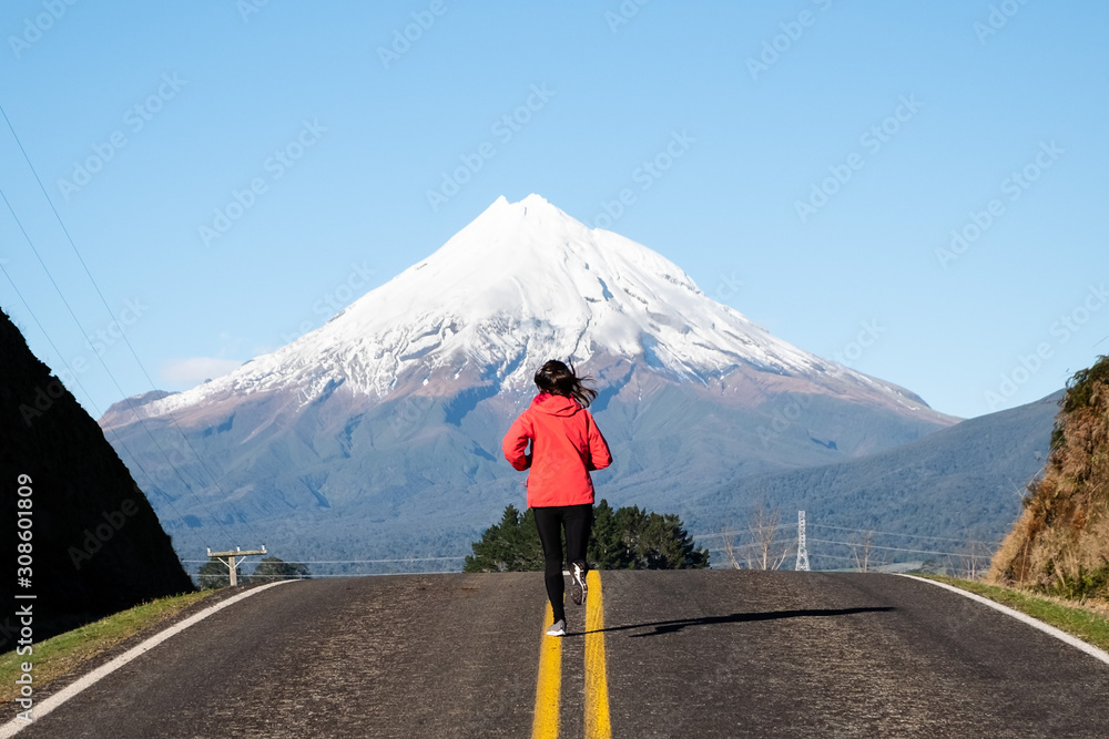Woman running on a straight road toward mountain. Motivation determined inspiration endurance concept 