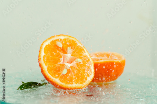 three orange tangerines with a branch and leaves stand in water on glass under drops of water on a white background copy space