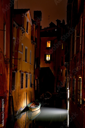 A resting boat in a canal in Venice, illuminated by some light. 