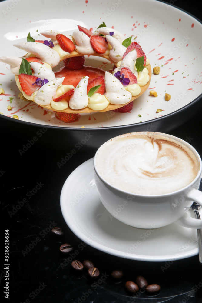 A cup of coffee served with beautifully decorated strawberry tart with lime meringue, exquisite restaurant dessert A cup of coffee served with beautifully decorated strawberry tart with lime meringue, exquisite restaurant dessert