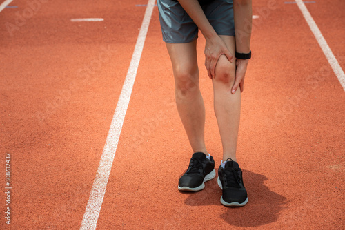 Shot of sport woman holding her knee, suffering from injury, she had bruise on her knee. Injured after runner falling or impact running track floor.