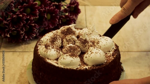 Woman cuts a piece of birthday homemade chocolate cake with cream and sponge cakes layers decorated fresh berries, closeup.