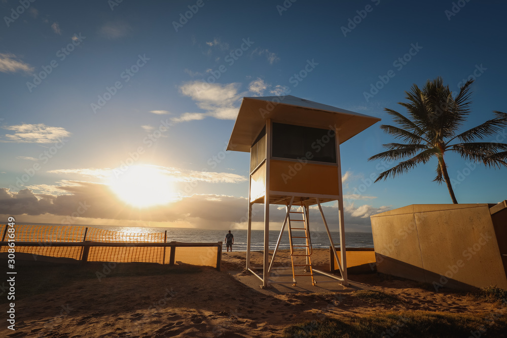 Lifeguard hut on the beach at sunrise with silhouette of a man watching the ocean Lifeguard hut on the beach at sunrise with silhouette of a man watching the ocean