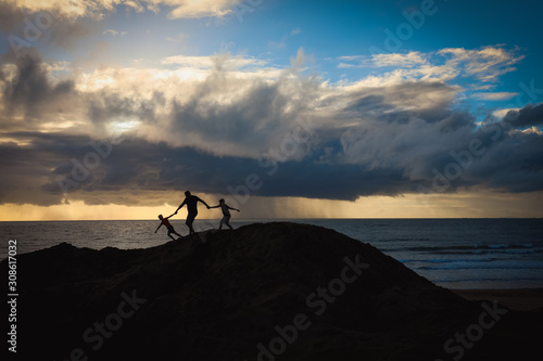 Silhouette of man and children on beach at sunrise with storm visible in the distance