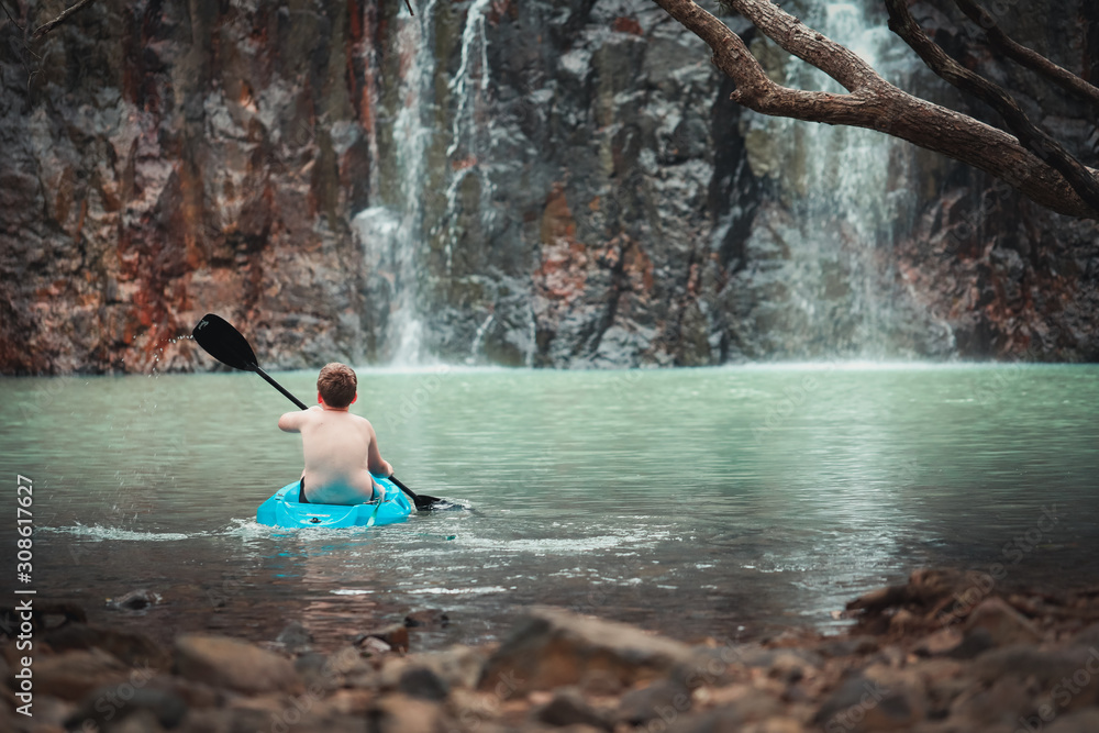 Young boy kayaking with paddle in cool blue water at Cedar Creek Falls near Airlie Beach in the Whitsundays, Queensland Australia Young boy kayaking with paddle in cool blue water at Cedar Creek Falls near Airlie Beach in the Whitsundays, Queensland Australia