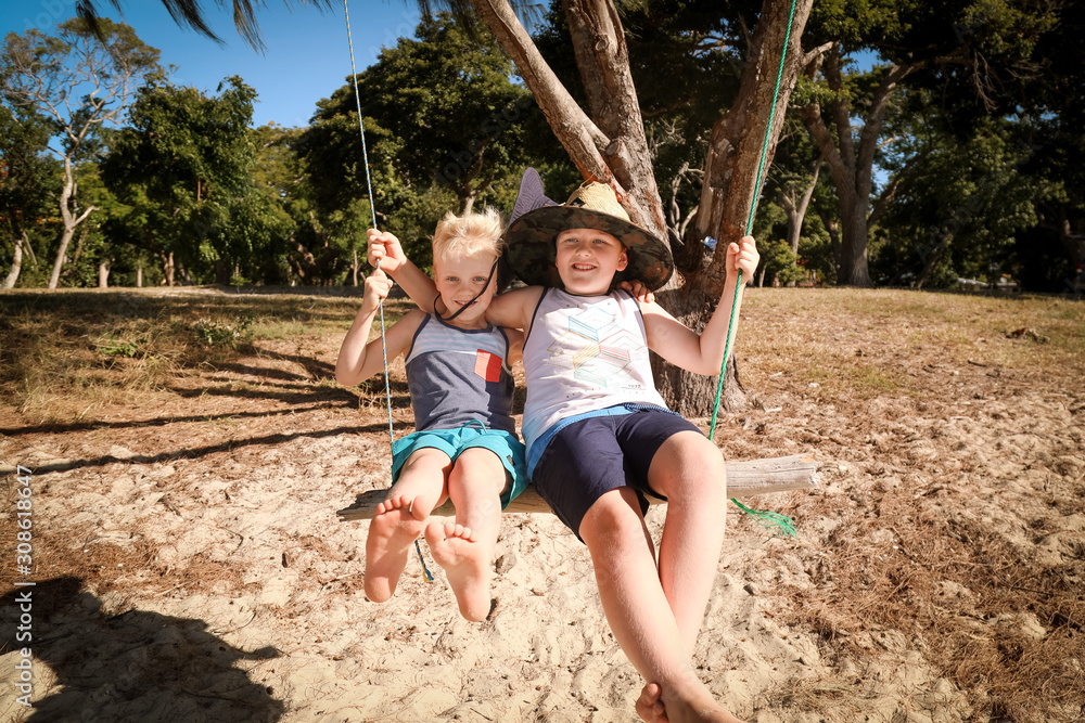 Boys swinging on homemade log swing at Dingo Beach, near Airlie Beach in the Whitsundays, Queensland Australia. Holiday fun with kids in paradise.
