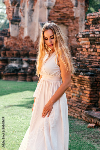 Portrait of stylish woman in white dress posing near beautiful Asian ancient building. Summer vacation, adventures concept. Vertical shot