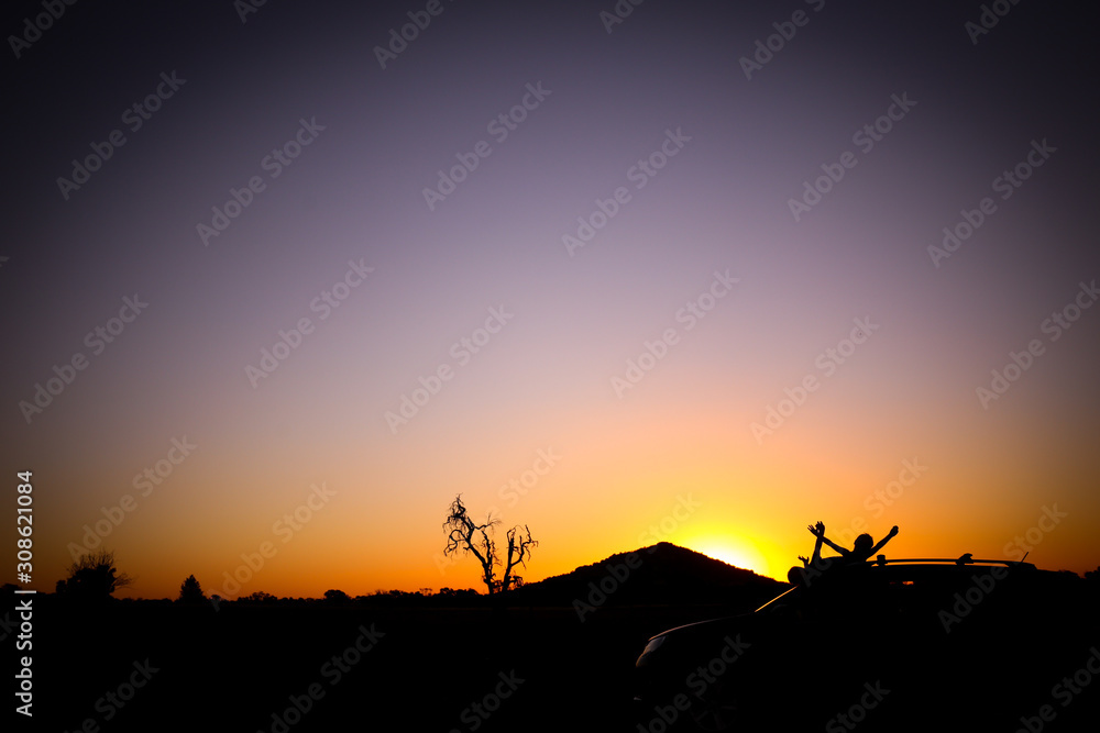 Silhouette of two children with arms up on top of a vehicle in front of Pyramid Hill in Victoria, Australia at sunset