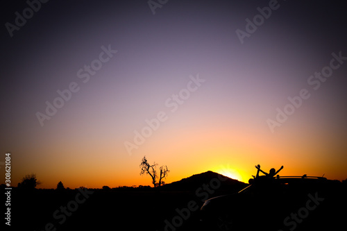 Silhouette of two children with arms up on top of a vehicle in front of Pyramid Hill in Victoria  Australia at sunset